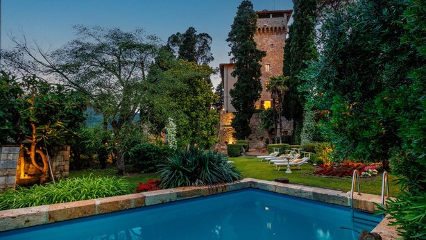 Una piscina rodeada de exuberante vegetación y un edificio de piedra con una torre.