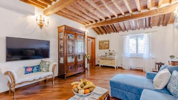Una sala de estar con techo de madera, un televisor de pantalla plana grande, un sofá azul, un sofá blanco y un mueble de madera.