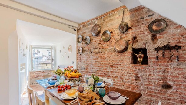 A dining area with a brick wall, a wooden table set with plates, bowls, and a variety of food items. - Casa La Guardia a 3 Bedrooms Panoramic Apartment (Lucca)