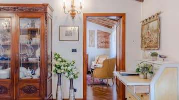 Una habitación con un armario de madera, dos jarrones con flores, una araña y un cuadro en la pared.