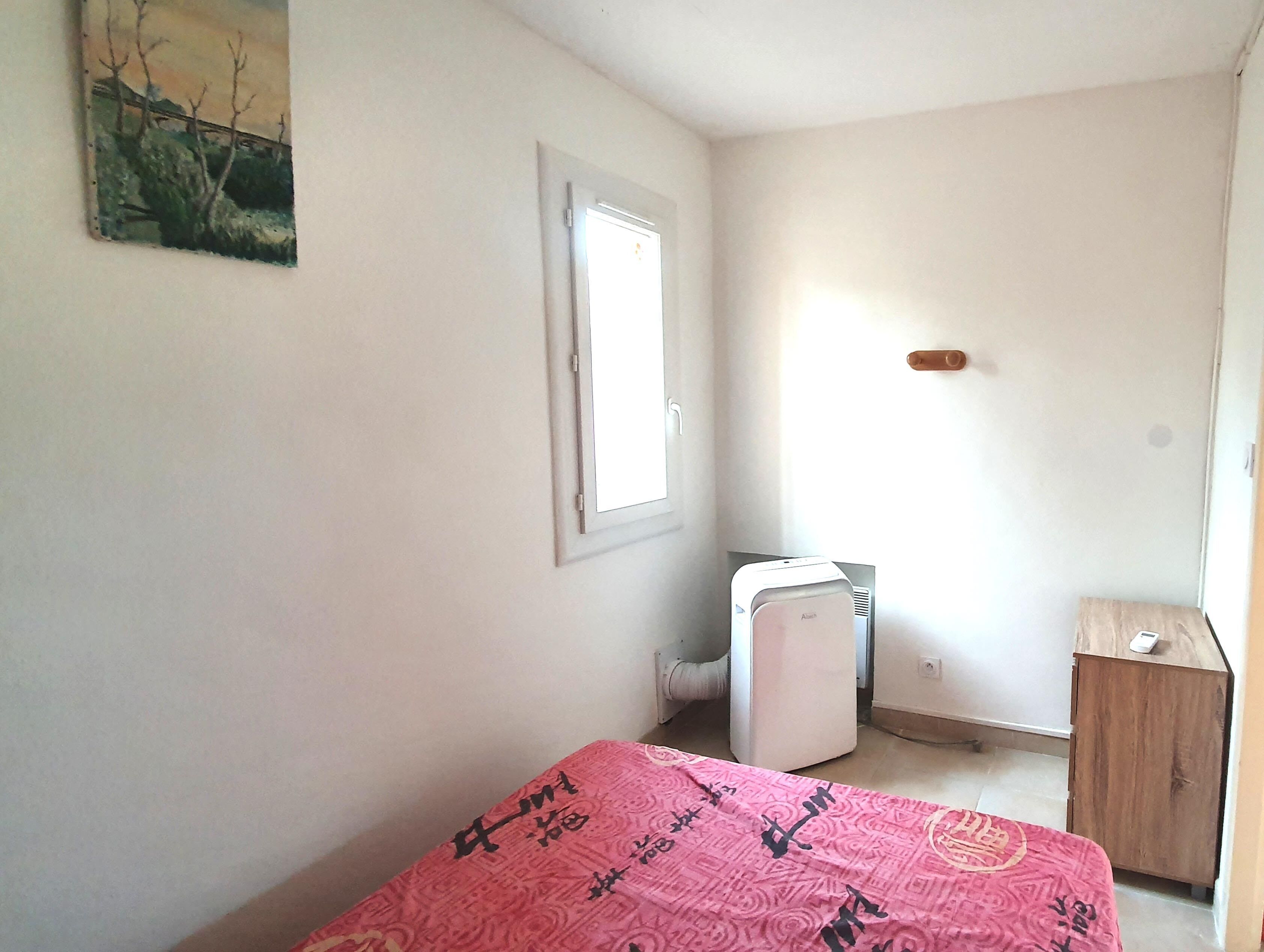 A small, sparsely furnished room with a bed, a radiator, and a wooden cabinet.