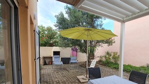 Une terrasse extérieure avec une table et des chaises, un parasol jaune et un sol en briques.