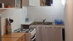 Une cuisine compacte équipée d’une cuisinière à gaz, d’un évier et d’un miroir au-dessus. On y trouve des étagères remplies de divers objets et un porte-serviettes suspendu.