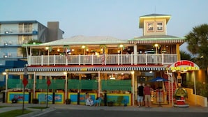 A two-story building with a bar and grill on the ground floor, featuring outdoor seating and a small play area for children. - $189 30 Steps from Beach l 3min Rest/Shops (Clearwater Beach)