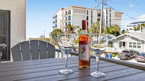 A table with a bottle of Barefoot wine and two empty wine glasses on a balcony with a view of a building and parked cars. - $189 30 Steps from Beach l 3min Rest/Shops (Clearwater Beach)