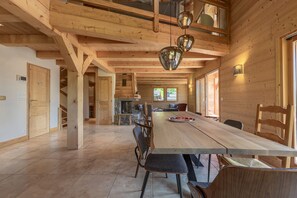 A spacious wooden interior with a long dining table, chairs, and a fireplace.