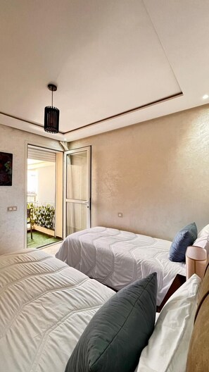 Quarto moderno com duas camas, luminária no teto e vista para uma varanda.