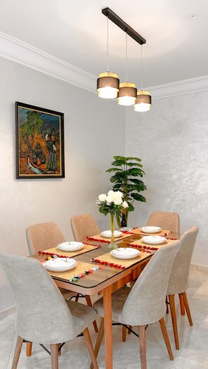 Uma área de jantar com mesa de vidro, seis cadeiras, um quadro na parede e um lustre.