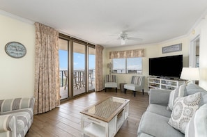 Relax in this stylish living room with a large flat-screen TV, comfortable seating, and a sliding glass door leading to a balcony with a view.
