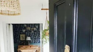 Une pièce avec une porte noire, un canapé jaune, une table basse en verre et un mur recouvert d’un papier peint à motifs.