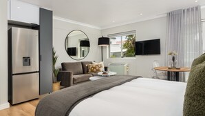 A modern hotel room with a bed, a sofa, a dining table, a TV, and a refrigerator. - Point Break | Studio | Kitchenette | Groundfloor (Cape Town)