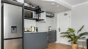 A modern kitchen with grey cabinets, a stainless steel refrigerator, and a built-in microwave. - Point Break | Ground Studio | Private Courtyard (Cape Town)