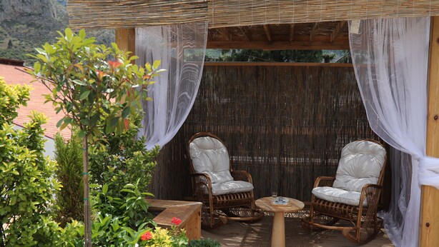 An outdoor seating area with wicker chairs and a small table, surrounded by greenery and a bamboo fence. - AFİLLİ KÖŞK (Amasya)