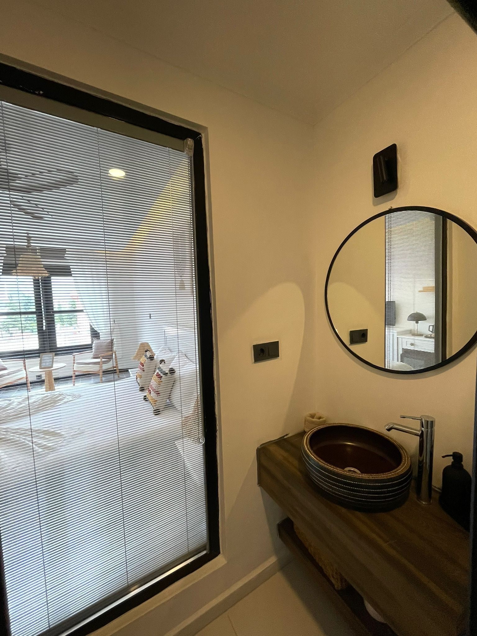 Un bagno con una grande finestra, uno specchio rotondo e un mobiletto in legno con lavabo a incasso.