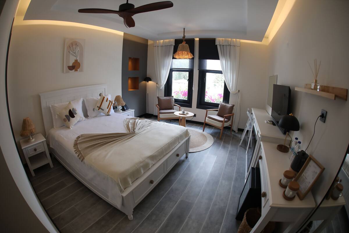 A modern bedroom with a large bed, a ceiling fan, a TV, and a desk with a chair.