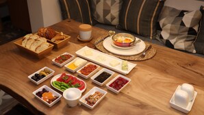 A wooden table with various food items and condiments, a bowl of bread, a cup, and a plate with a baked dish. - AFİLLİ KÖŞK (Amasya)