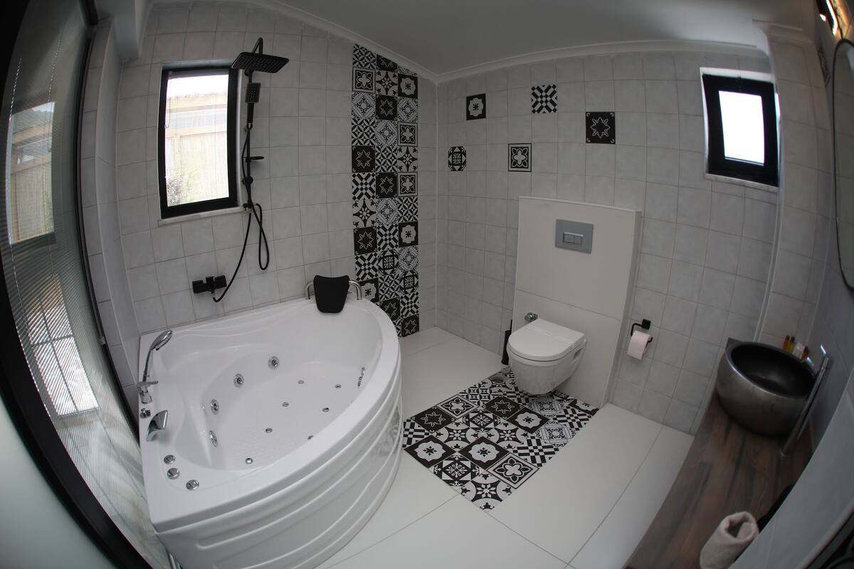A modern bathroom with a freestanding bathtub, a toilet, and a bidet. The floor has patterned tiles, and there are decorative tiles on the walls.