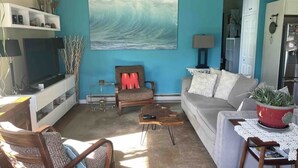 Ein Wohnzimmer mit einem großen Wandbild einer Welle, einem Sofa, einem Sessel, einem Couchtisch und einem Fernseher.
