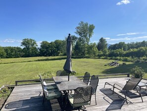 Eine Terrasse mit Tisch und Stühlen, mit Blick auf ein Wiesenfeld und Bäume.