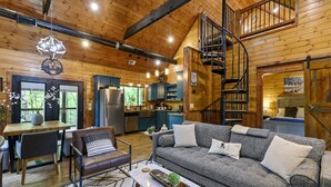A spacious living area with a gray sofa, a wooden dining table, and a staircase leading to an upper level.