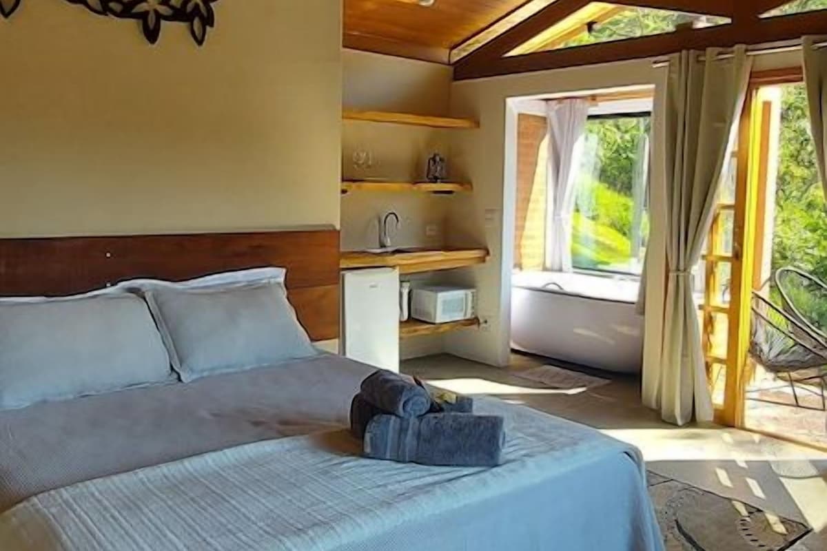 A bedroom with a bed, a small bedside table, a wall-mounted air conditioner, and a view of the outdoors.