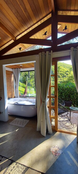 Una stanza con un'ampia finestra, vista sul verde circostante, soffitto in legno e una vasca da bagno.