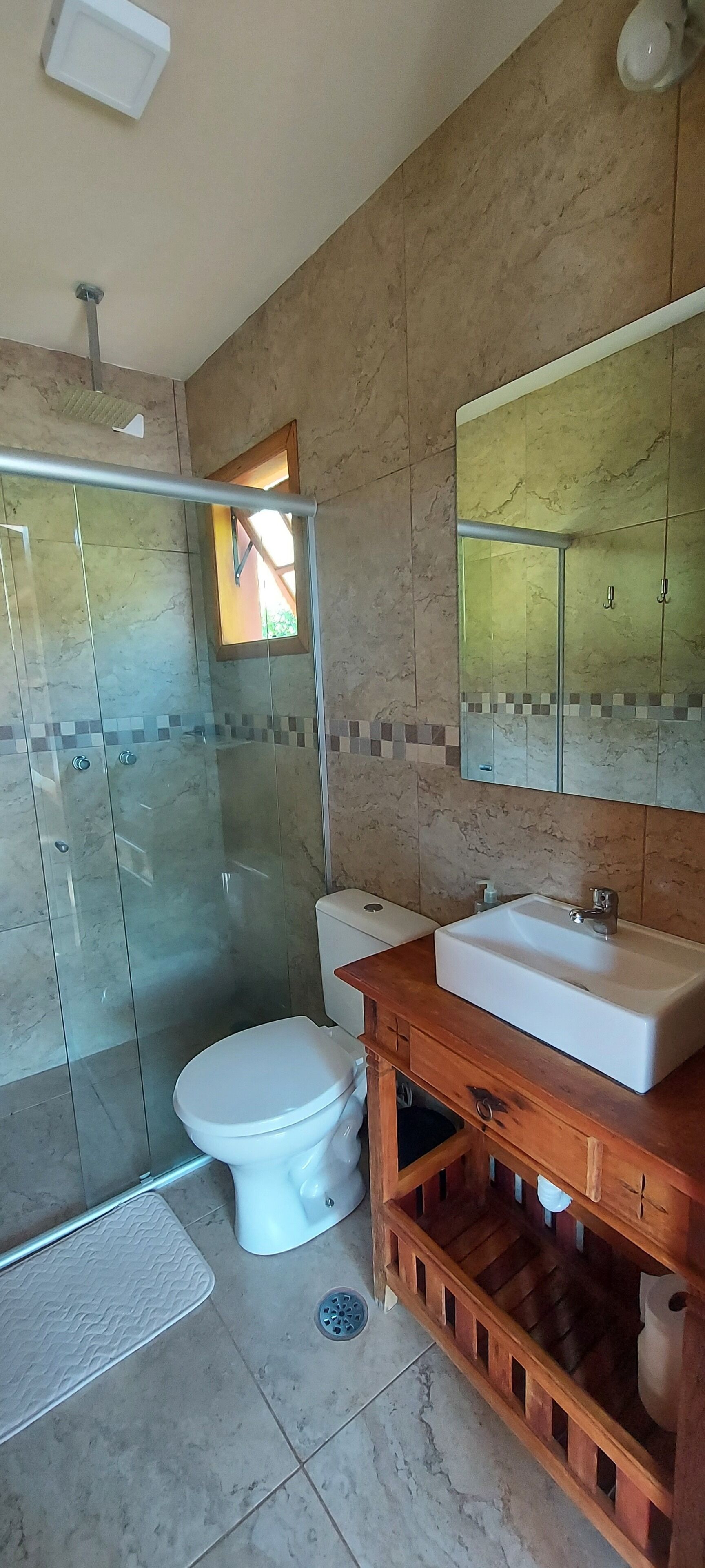 A modern bathroom with a glass shower enclosure, a white toilet, a wooden vanity with a sink, and a large mirror above the vanity.