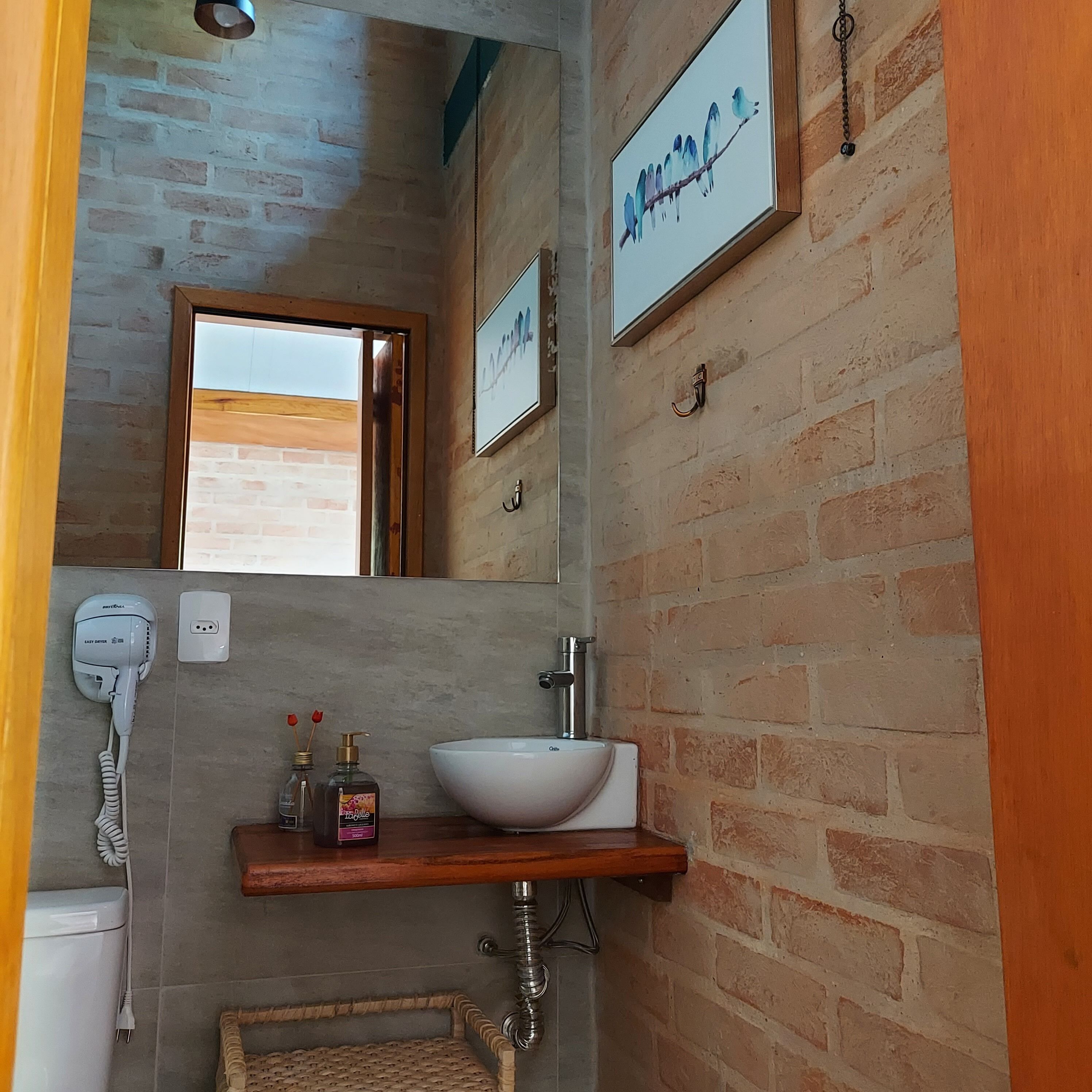 A bathroom with a wooden vanity, a white sink, a hairdryer, and a mirror.