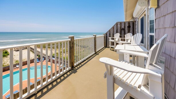 Un balcone con sedie bianche, una piscina e vista sull'oceano.