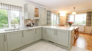 A modern kitchen with light-colored cabinets, a built-in oven, and a large window providing natural light. - Hefo'r Grug (Pwllheli)