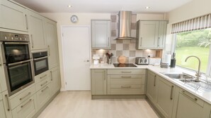 A modern kitchen with two ovens, a toaster, a sink, and a window with a view of greenery. - Hefo'r Grug (Pwllheli)