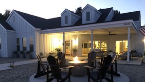 A covered outdoor seating area with Adirondack chairs and a fire pit, surrounded by a gravel patio. - Lux Vineyard Escapes-Ultimate Modern Farm House (Temecula)
