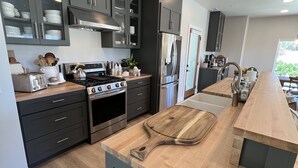 A modern kitchen with dark cabinets, stainless steel appliances, and a wooden island. - Lux Vineyard Escapes-Ultimate Modern Farm House (Temecula)