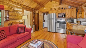 L’intérieur chaleureux d’un chalet en bois comprend un canapé rouge, un plancher en bois, une cuisine équipée d’appareils électroménagers en acier inoxydable et un coin repas.