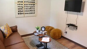 Un salon avec un canapé marron, une table basse, un téléviseur fixé au mur et un tapis à motifs.