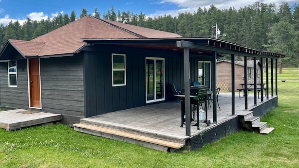 Une maison aux couleurs sombres, dotée d’un porche abrité, d’une terrasse en bois et d’une cour gazonnée.