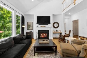 A living room with a fireplace, a black sofa, a coffee table, and a television mounted above the fireplace.