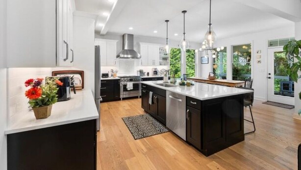 Une cuisine moderne dotée d’un îlot central, d’appareils électroménagers en acier inoxydable, de luminaires suspendus et offrant une vue sur la verdure environnante.