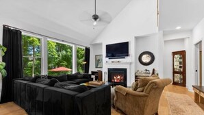 Ein modernes Wohnzimmer mit einem schwarzen Ecksofa, einem braunen Sessel, einem Kamin und einem an der Wand montierten Fernseher.