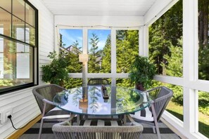 A glass-top table with wicker chairs in a covered outdoor area with white walls and large windows.