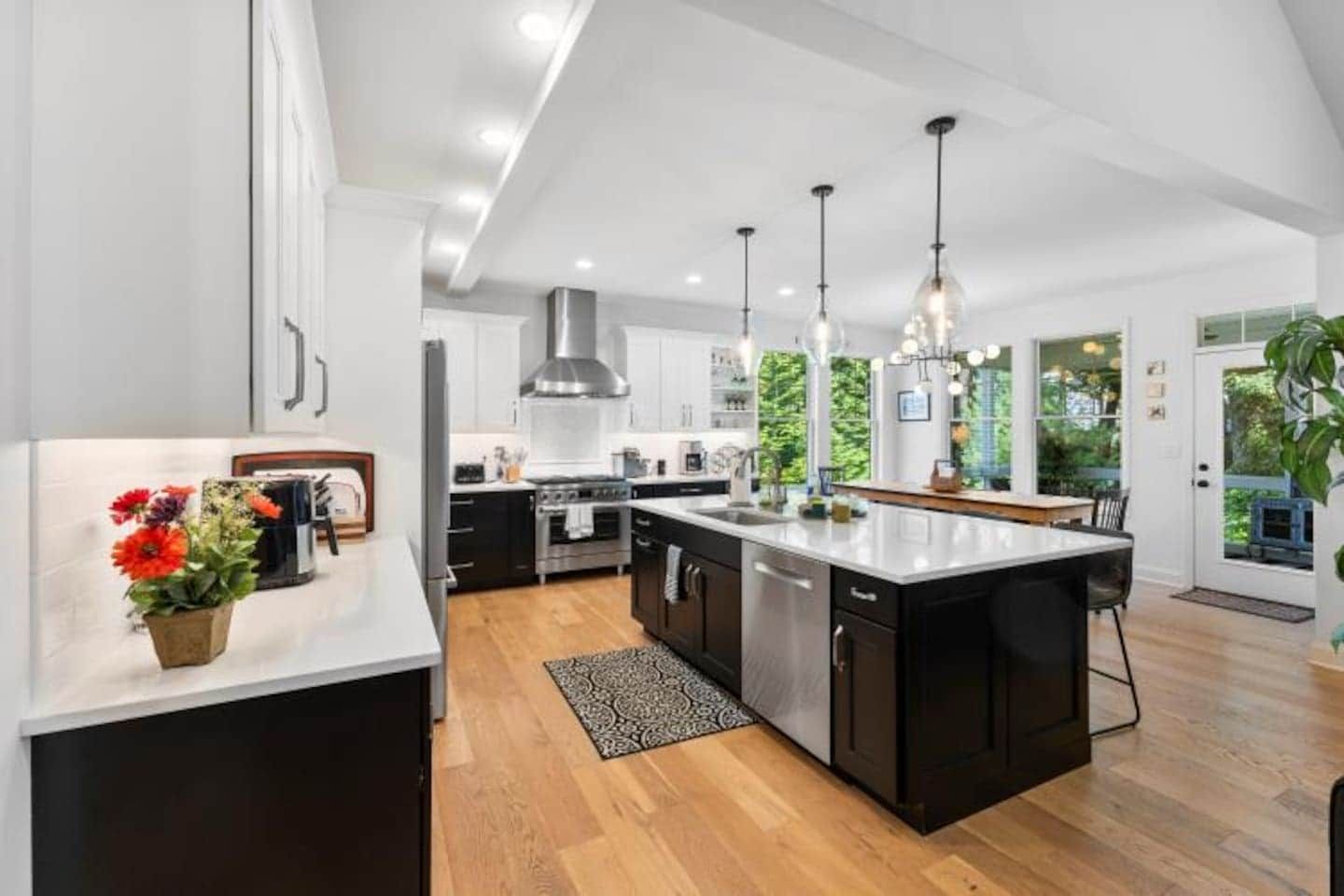 Una cocina moderna con una isla central, electrodomésticos de acero inoxidable, iluminación colgante y vistas a zonas verdes.