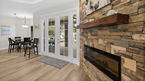 A dining area with a table and chairs, a fireplace, and a view through glass doors to an outdoor patio.