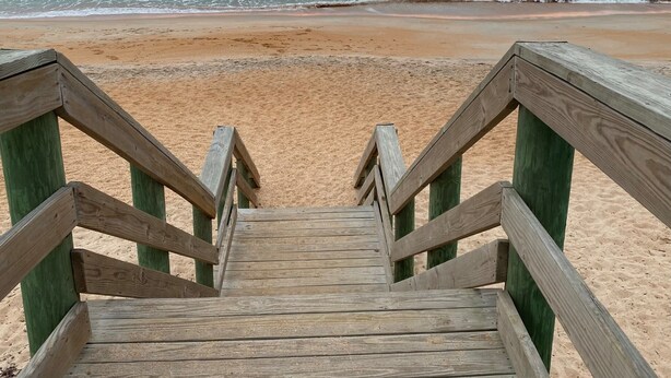 A wooden staircase leading to a sandy beach with the ocean in the background.