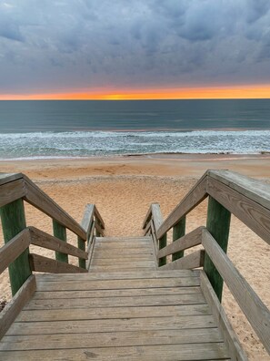 A wooden staircase leading to a sandy beach with the ocean in the background.