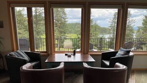 Huoneessa on puinen pöytä ja kaksi nahkaista tuolia, ja suurista ikkunoista avautuu näkymä parvekkeelle ja puille.