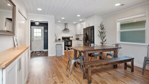 A modern kitchen with white cabinets, a wooden dining table, and a built-in oven. - Beach Please: Modern Coastal Bungalow Near Waterway and Marshwalk (Oak Island)