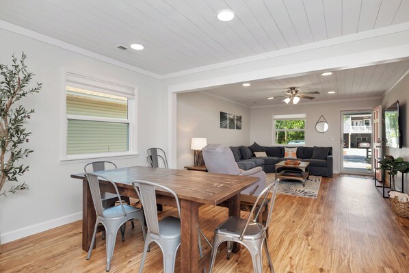 A spacious living area with a wooden dining table, grey chairs, a grey sofa, and a ceiling fan.