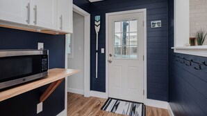 A modern kitchen with white cabinets, a microwave, and a wooden shelf. - Beach Please: Modern Coastal Bungalow Near Waterway and Marshwalk (Oak Island)