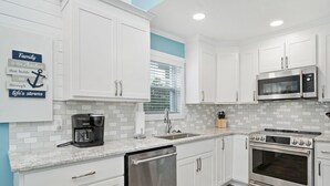 A modern kitchen with white cabinets, a stainless steel dishwasher, a built-in oven, and a microwave. - A Pier to Sea: Elegant Home with Private Pool, Hot Tub, Expansive Deck (Oak Island)