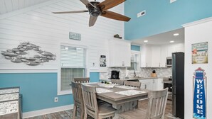 A modern kitchen with white cabinets, a black refrigerator, and a wooden dining table with chairs. - A Pier to Sea: Elegant Home with Private Pool, Hot Tub, Expansive Deck (Oak Island)